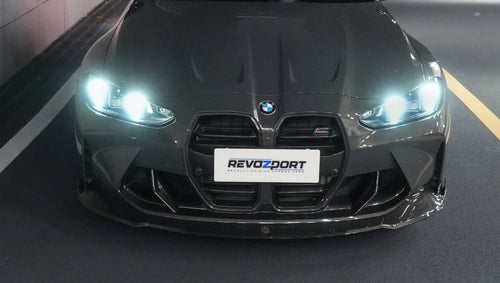 Gray BMW G80 M3 featuring a REVOZPORT carbon fiber front lip, side skirts, bronze wheels, and M The M3 side graphics driving through a tunnel at night.