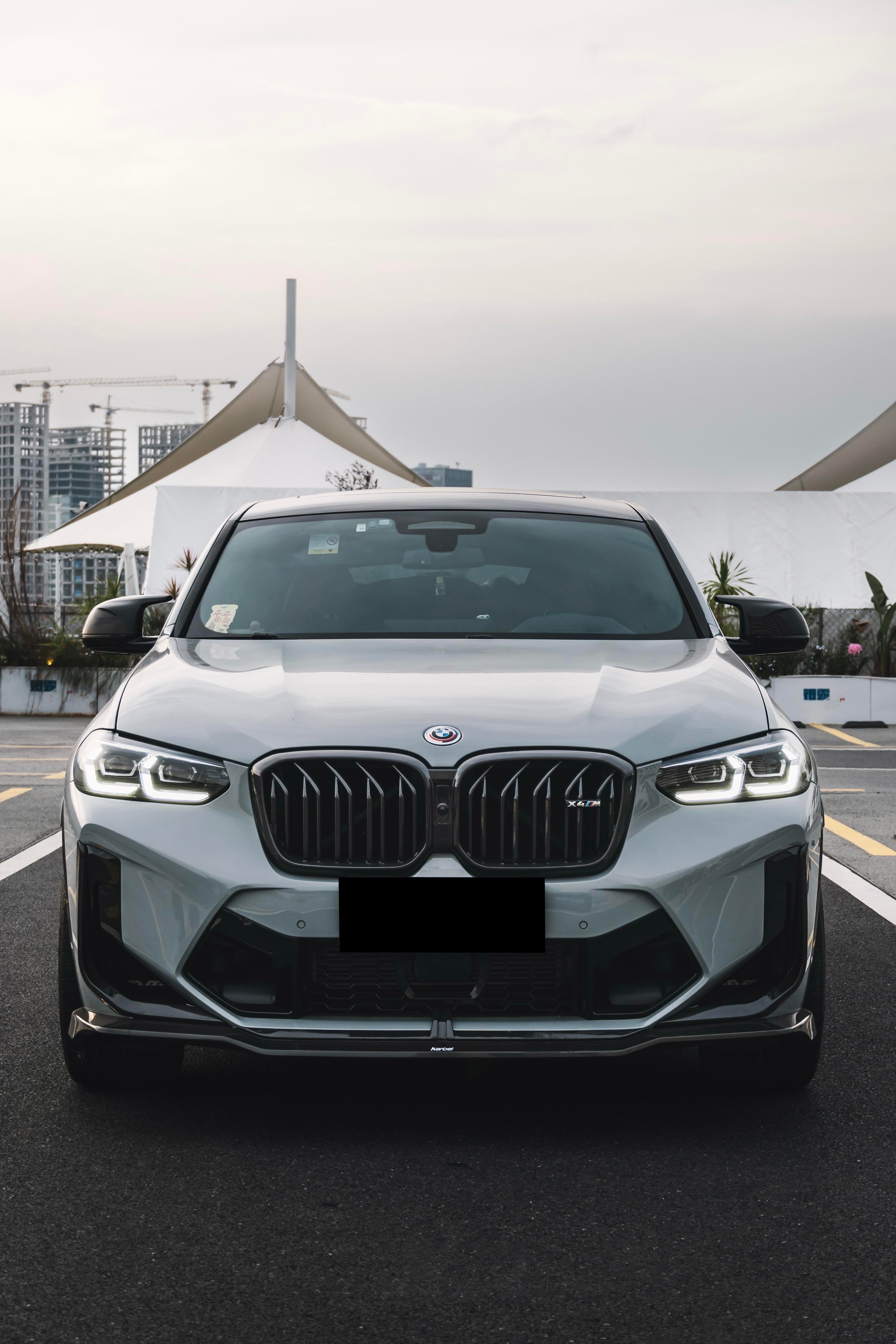 White BMW X4M featuring a REVOZPORT front grille upgrade and sporty front-end styling parked on an open urban road.