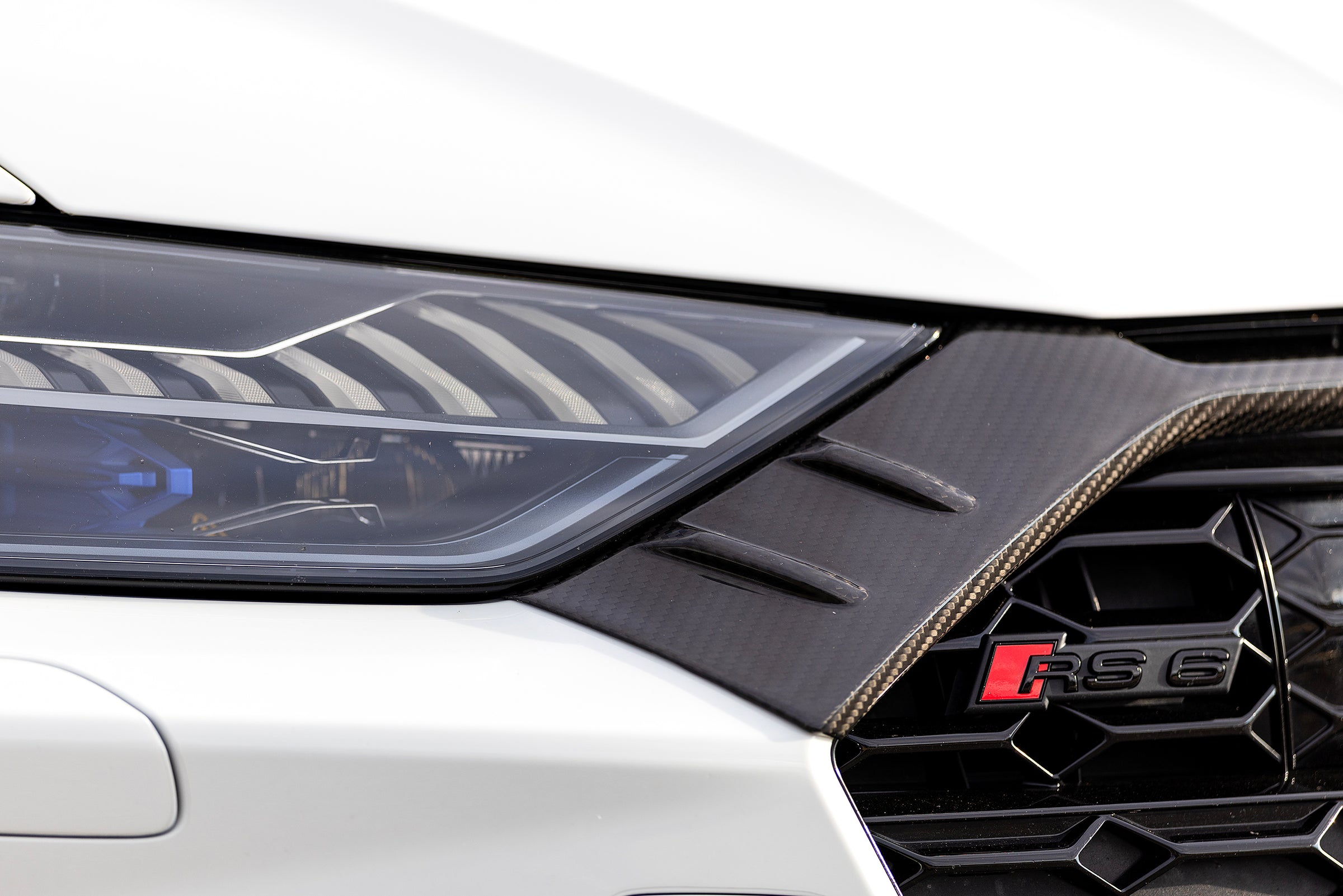 White Audi RS6 Avant featuring a REVOZPORT carbon fiber body kit with front lip, side skirts, rear diffuser, and lowered stance parked in a modern urban waterfront setting.