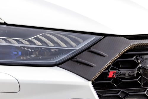 White Audi RS6 Avant featuring a REVOZPORT carbon fiber body kit with front lip, side skirts, rear diffuser, and lowered stance parked in a modern urban waterfront setting.