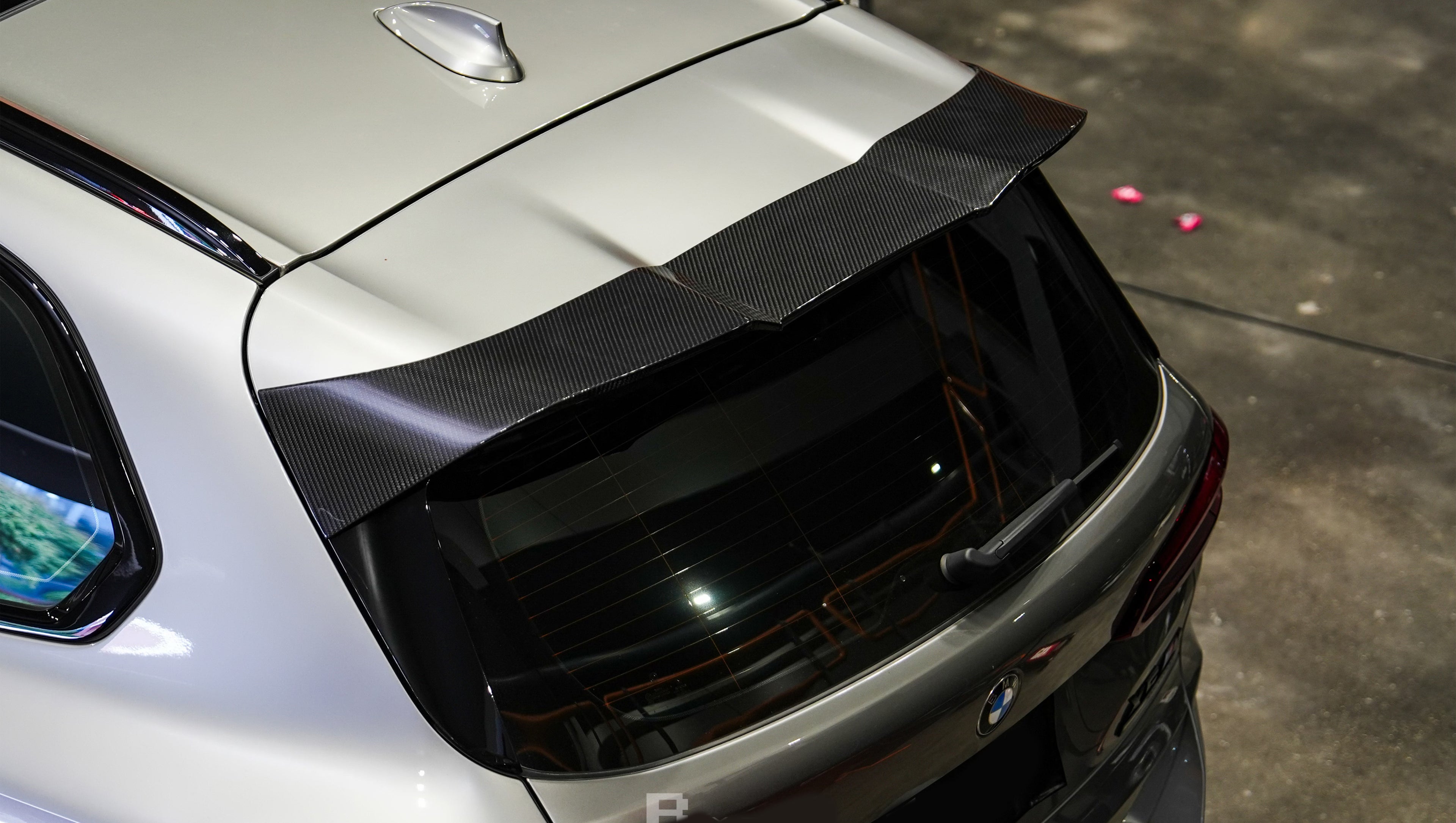 Gray BMW X5M featuring a REVOZPORT carbon fiber body kit with aggressive front lip, enlarged air intakes, side skirts, and sporty aero styling displayed inside a performance workshop.
