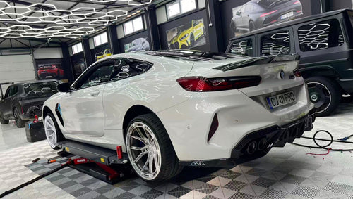 White BMW F92 M8 featuring a REVOZPORT carbon fiber front lip, side skirts, black front grille, and white multi-spoke forged wheels parked at sunset on an open road.