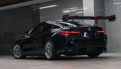 Dark blue BMW G82 M4 equipped with carbon fiber front splitter, side skirts, vented fenders, and a large rear wing, parked inside a modern luxury garage.