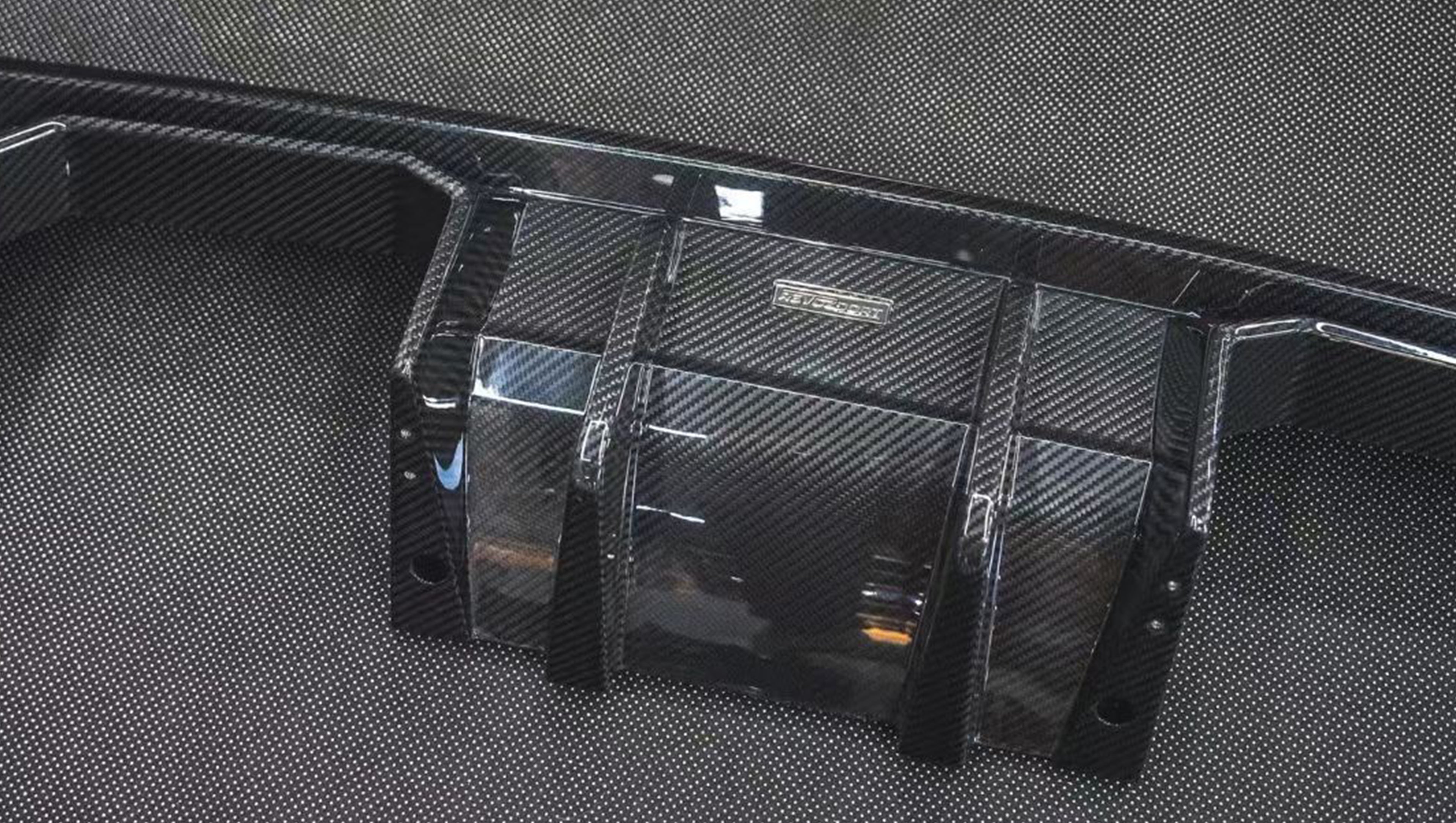 REVOZPORT glossy carbon fiber body kit components displayed before installation, including front lip sections, side skirts, rear diffuser, and aero trim pieces.