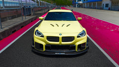 Yellow BMW G82 M4 with aggressive carbon fiber front splitter, vented hood, side canards, and bronze wheels parked on a race track pit lane.