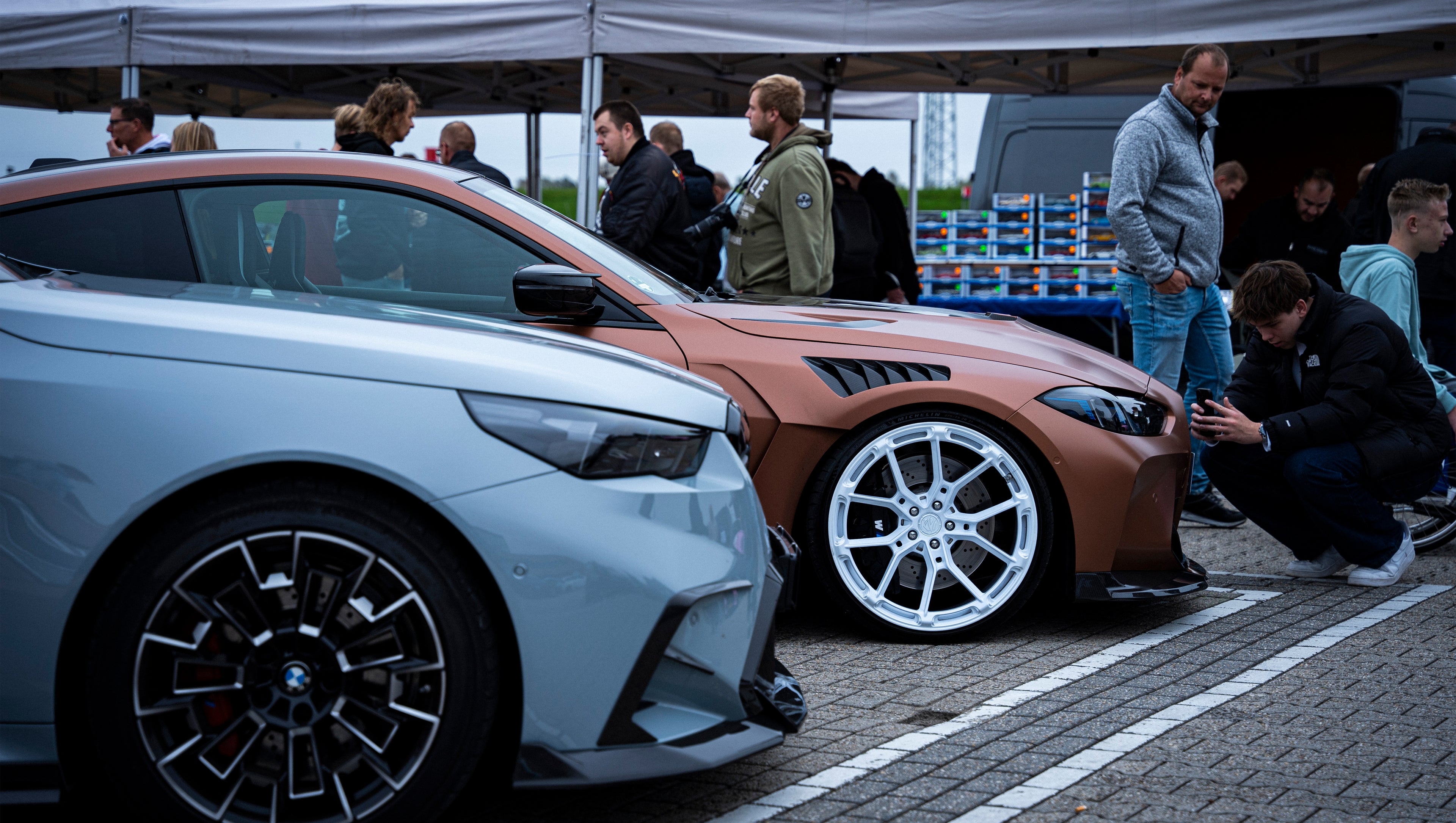 Gray BMW G90 M5 Touring featuring a REVOZPORT carbon fiber front lip, aggressive front aero styling, and black grille displayed at a car event.