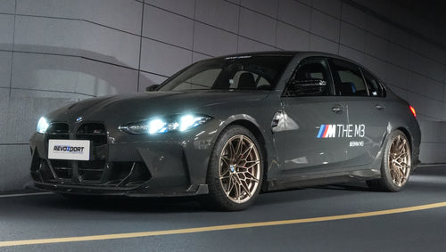 Gray BMW G80 M3 featuring a REVOZPORT carbon fiber front lip, side skirts, bronze wheels, and M The M3 side graphics driving through a tunnel at night.