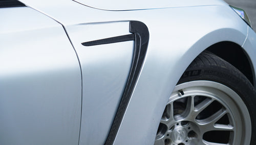 Front view of a silver BMW G87 M2 featuring a REVOZPORT carbon fiber front lip, aggressive front bumper aero styling, and vented hood parked on an urban street.