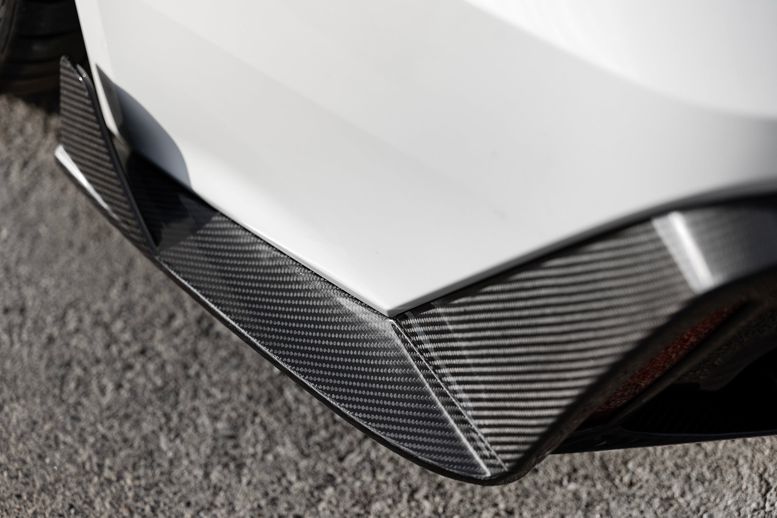 White Audi RS6 Avant featuring a REVOZPORT carbon fiber body kit with front lip, side skirts, rear diffuser, and lowered stance parked in a modern urban waterfront setting.