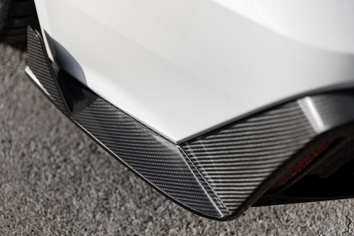 White Audi RS6 Avant featuring a REVOZPORT carbon fiber body kit with front lip, side skirts, rear diffuser, and lowered stance parked in a modern urban waterfront setting.