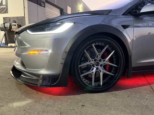 Tesla Model X featuring an aggressive REVOZPORT carbon fiber body kit with front lip, vented hood, wide fender extensions, side skirts, and illuminated red underglow lighting at dusk.