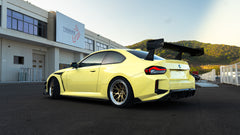 Rear three-quarter view of a BMW featuring oversized carbon fiber rear wing, aggressive widebody styling, bronze forged wheels, and track-focused aero details.