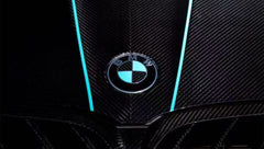 Turquoise BMW F92 M8 featuring a REVOZPORT carbon fiber body kit with front lip, side skirts, black hood accents, side vents, and silver forged wheels parked outside an industrial loading dock.