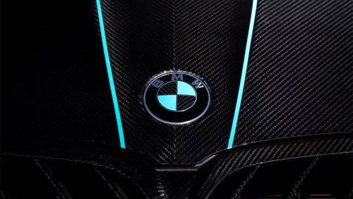 Turquoise BMW F92 M8 featuring a REVOZPORT carbon fiber body kit with front lip, side skirts, black hood accents, side vents, and silver forged wheels parked outside an industrial loading dock.