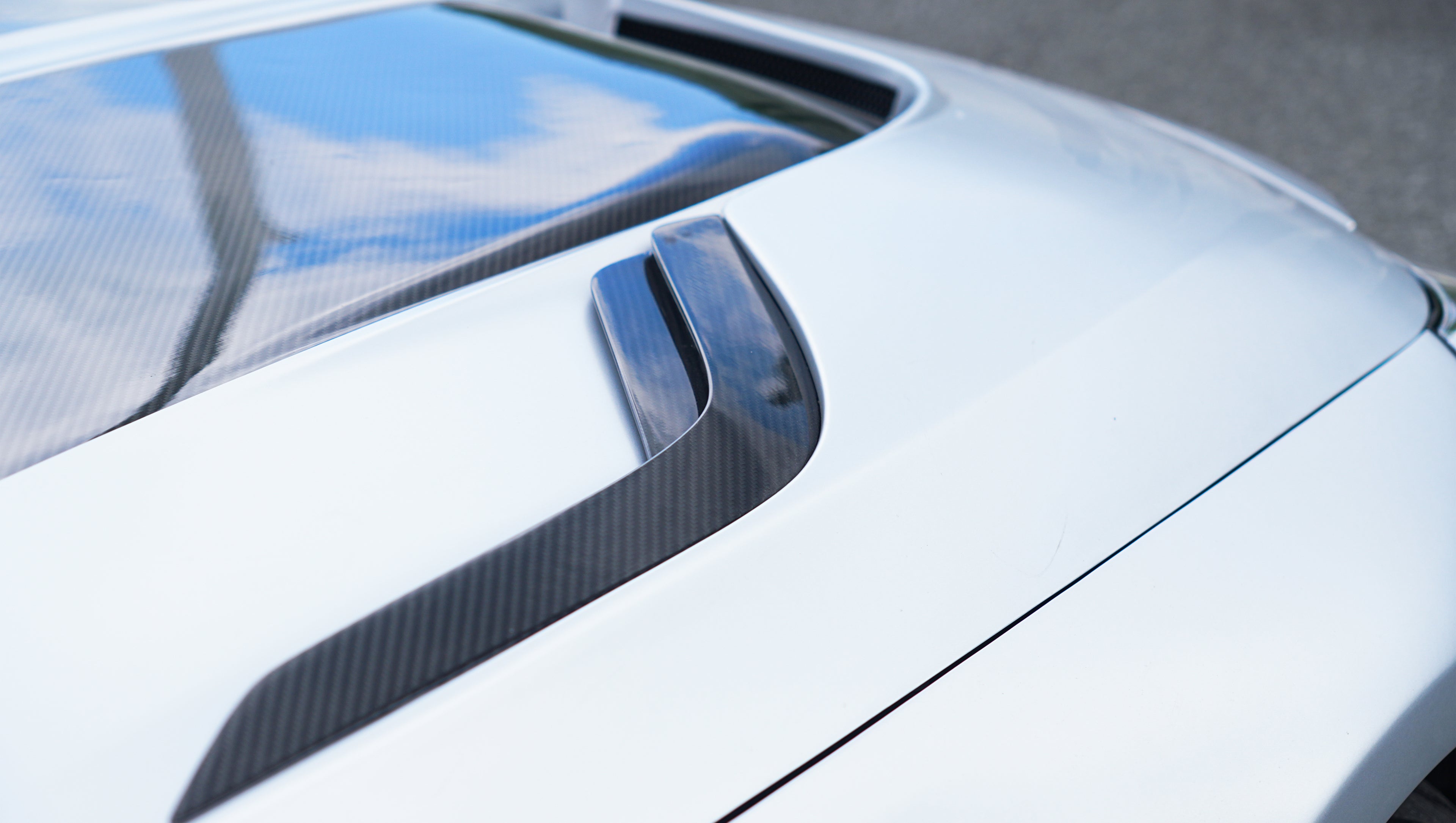 Front view of a silver BMW G87 M2 featuring a REVOZPORT carbon fiber front lip, aggressive front bumper aero styling, and vented hood parked on an urban street.