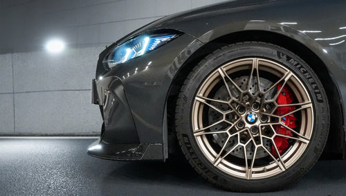 Gray BMW G80 M3 featuring a REVOZPORT carbon fiber front lip, side skirts, bronze wheels, and M The M3 side graphics driving through a tunnel at night.