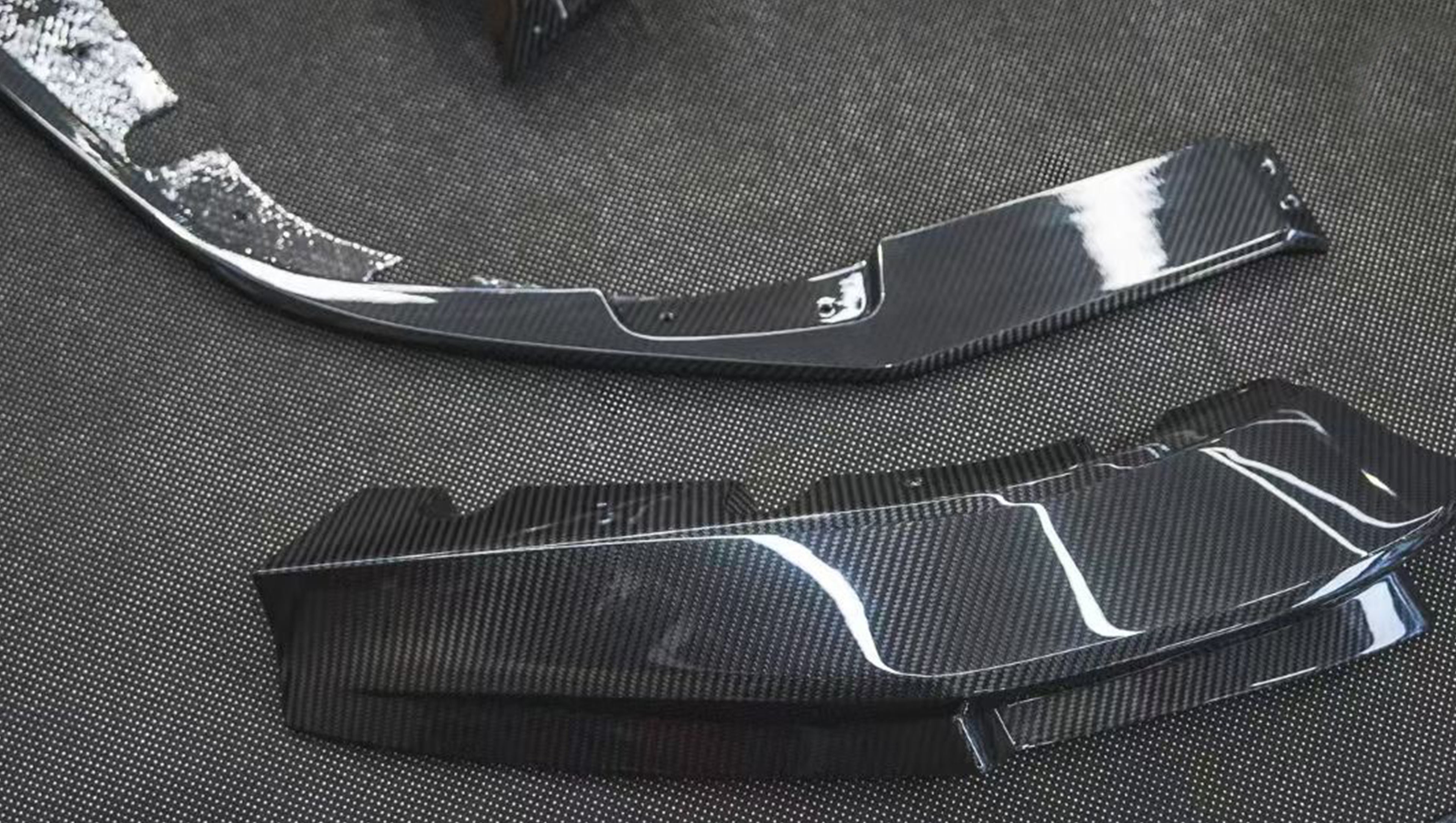 REVOZPORT glossy carbon fiber body kit components displayed before installation, including front lip sections, side skirts, rear diffuser, and aero trim pieces.