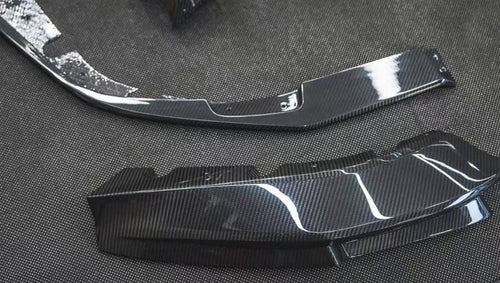 REVOZPORT glossy carbon fiber body kit components displayed before installation, including front lip sections, side skirts, rear diffuser, and aero trim pieces.