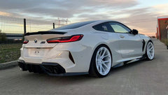 White BMW F92 M8 featuring a REVOZPORT carbon fiber front lip, side skirts, black front grille, and white multi-spoke forged wheels parked at sunset on an open road.