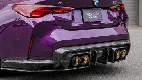 Purple BMW G82 M4 featuring a REVOZPORT carbon fiber body kit with front lip, side skirts, vented fenders, and gold wheels parked outside a modern industrial building.