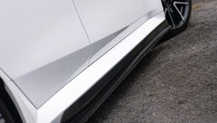 White BMW G90 M5 featuring a REVOZPORT carbon fiber front lip, side skirts, and aggressive front aero styling parked in a natural outdoor setting.