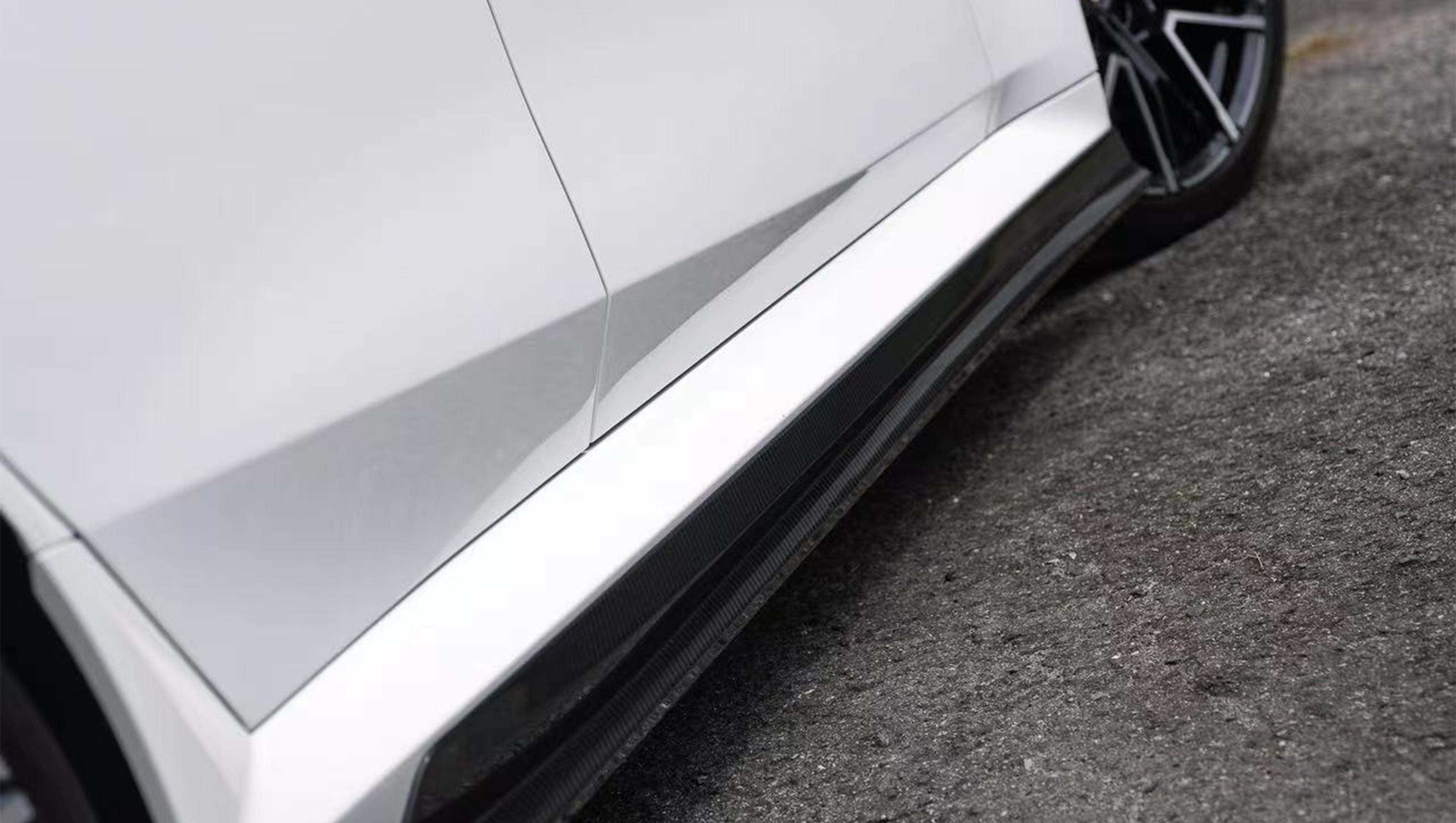 White BMW G90 M5 featuring a REVOZPORT carbon fiber front lip, side skirts, and aggressive front aero styling parked in a natural outdoor setting.