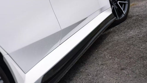 White BMW G90 M5 featuring a REVOZPORT carbon fiber front lip, side skirts, and aggressive front aero styling parked in a natural outdoor setting.