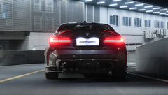 Gray BMW G80 M3 featuring a REVOZPORT carbon fiber front lip, side skirts, bronze wheels, and M The M3 side graphics driving through a tunnel at night.