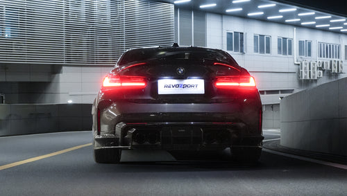 Gray BMW G80 M3 featuring a REVOZPORT carbon fiber front lip, side skirts, bronze wheels, and M The M3 side graphics driving through a tunnel at night.