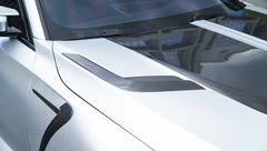 Front view of a silver BMW G87 M2 featuring a REVOZPORT carbon fiber front lip, aggressive front bumper aero styling, and vented hood parked on an urban street.