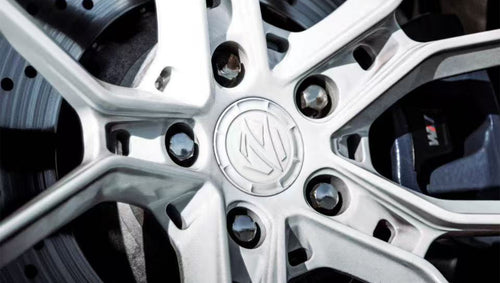 Close-up of a white REVOZPORT forged wheel with multi-spoke design, black lug nuts, and visible performance brake rotor behind the spokes.