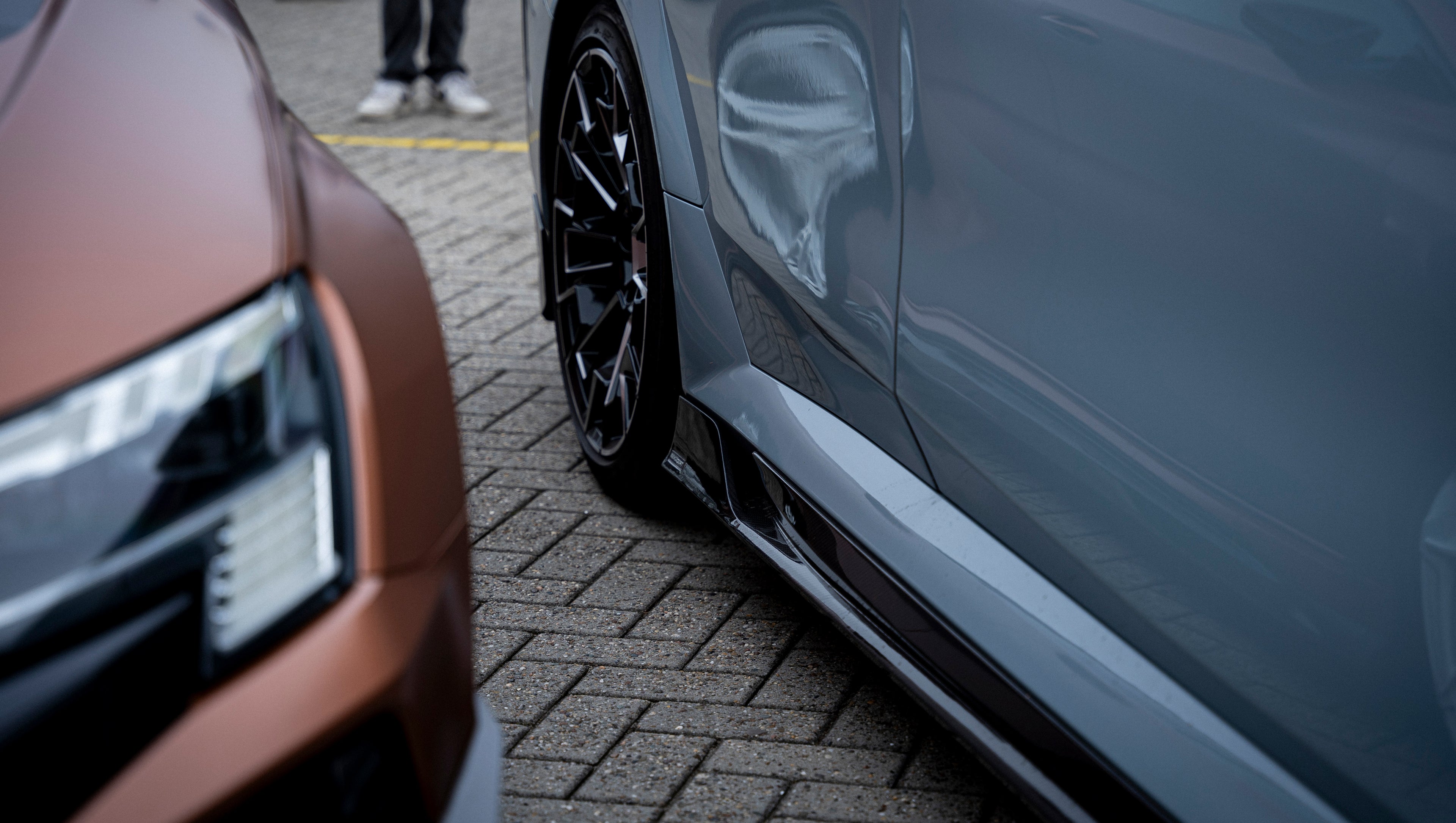 Gray BMW G90 M5 Touring featuring a REVOZPORT carbon fiber front lip, aggressive front aero styling, and black grille displayed at a car event.