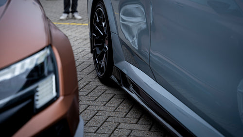 Gray BMW G90 M5 Touring featuring a REVOZPORT carbon fiber front lip, aggressive front aero styling, and black grille displayed at a car event.