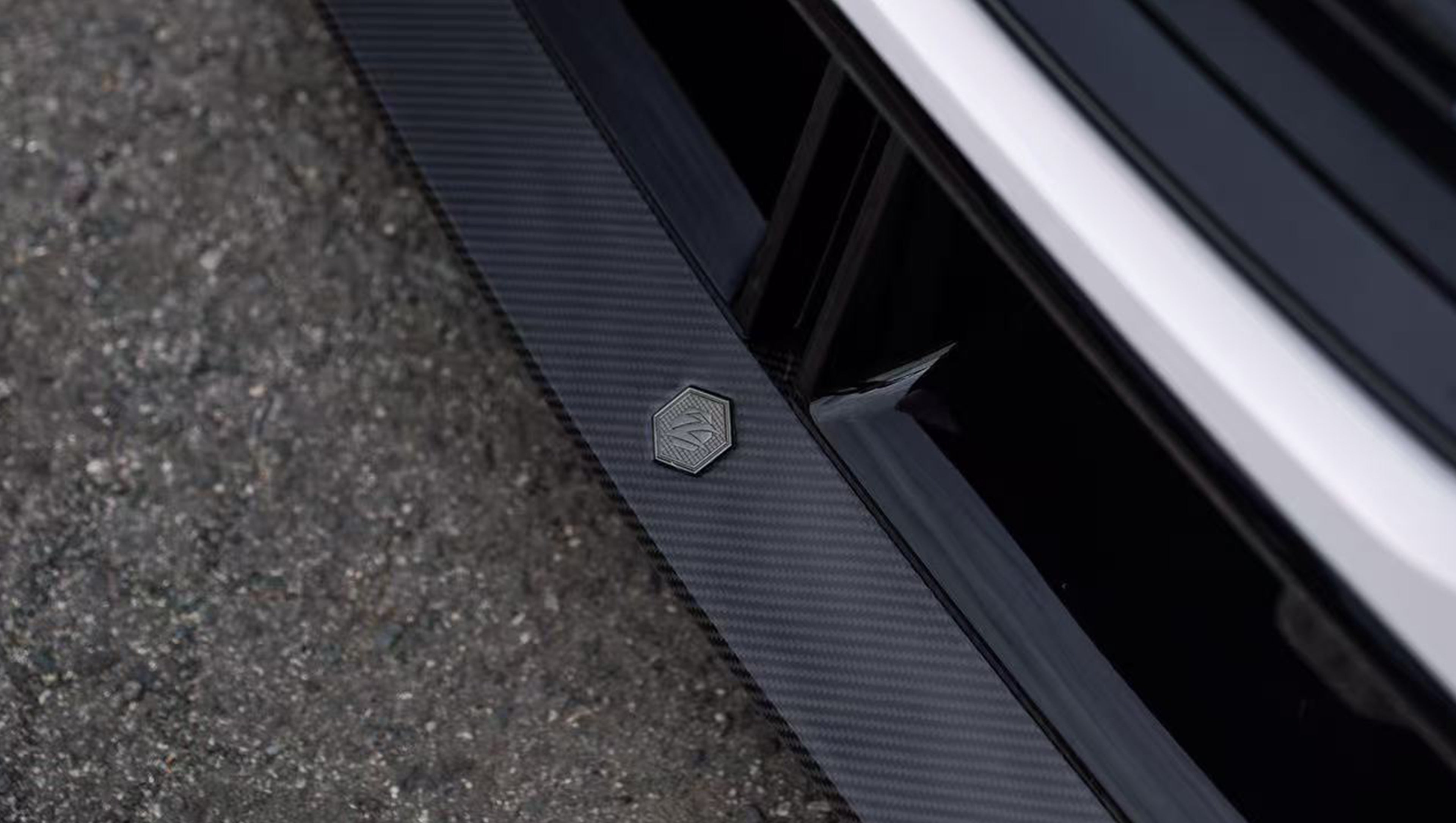 White BMW G90 M5 featuring a REVOZPORT carbon fiber front lip, side skirts, and aggressive front aero styling parked in a natural outdoor setting.