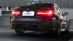 Rear view of a black BMW G80 M3 featuring a REVOZPORT carbon fiber rear diffuser and aggressive rear aero styling, with LED taillights illuminated inside a modern garage.