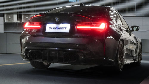 Rear view of a black BMW G80 M3 featuring a REVOZPORT carbon fiber rear diffuser and aggressive rear aero styling, with LED taillights illuminated inside a modern garage.