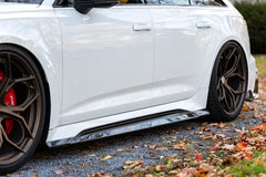 White Audi RS6 Avant featuring a REVOZPORT carbon fiber body kit with front lip, side skirts, and aggressive aero styling parked in front of a historic stone mansion during autumn.