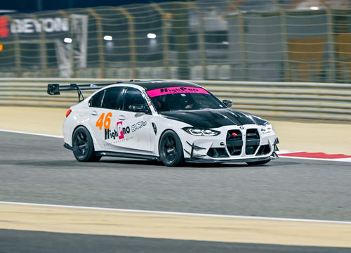White BMW G80 M3 track car with REVOZPORT carbon fiber aero kit, front canards, rear wing, and racing decals driving on a professional race circuit.