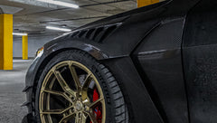 Close-up of a matte black BMW G82 M4 featuring REVOZPORT carbon fiber vented fenders, carbon side skirts, bronze forged wheels, and red performance brakes.