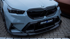 Gray BMW G90 M5 Touring featuring a REVOZPORT carbon fiber front lip, aggressive front aero styling, and black grille displayed at a car event.