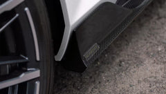 White BMW G90 M5 featuring a REVOZPORT carbon fiber front lip, side skirts, and aggressive front aero styling parked in a natural outdoor setting.