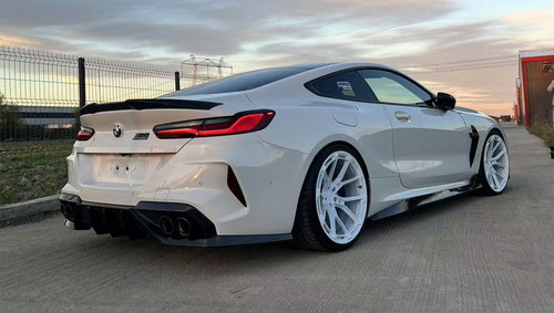 White BMW F92 M8 featuring a REVOZPORT carbon fiber front lip, side skirts, black front grille, and white multi-spoke forged wheels parked at sunset on an open road.