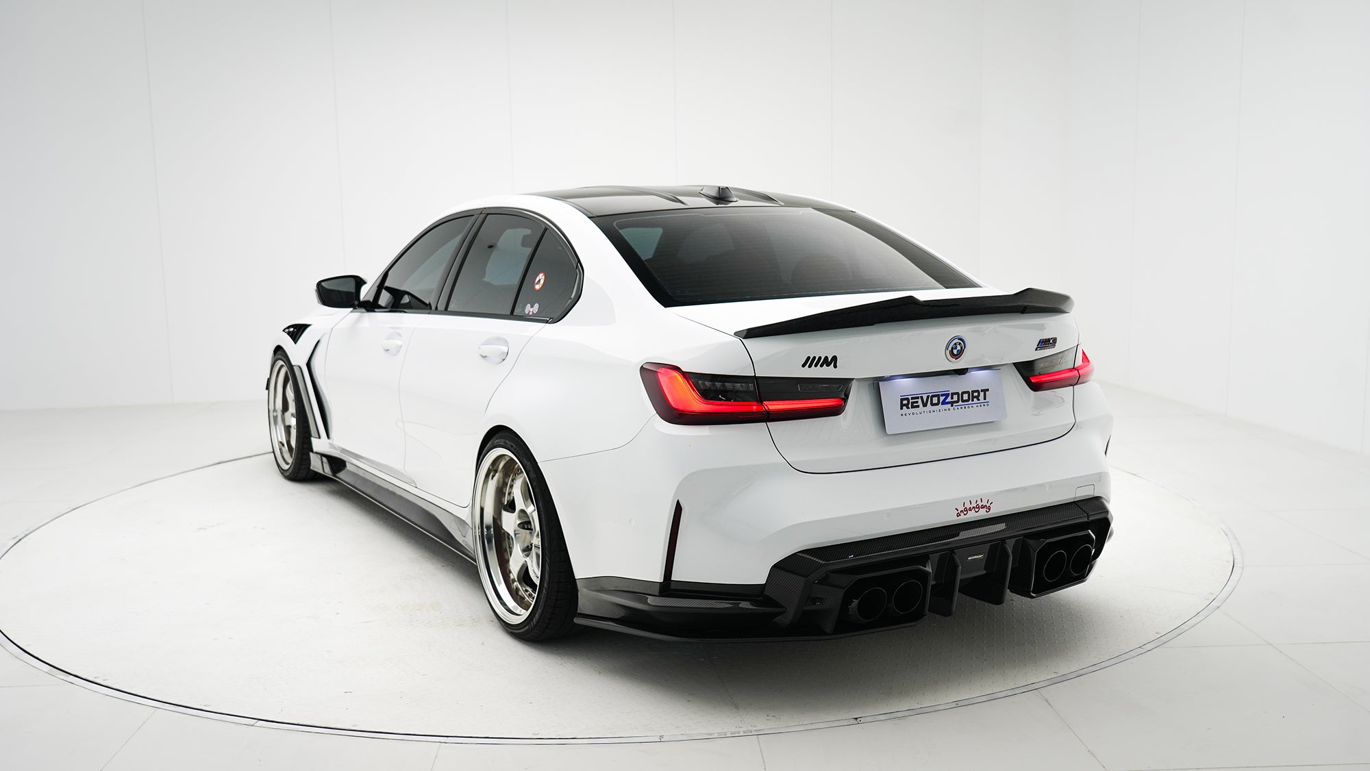White BMW G80 M3 featuring a REVOZPORT carbon fiber body kit with front lip, side skirts, canards, vented fenders, and yellow DRL headlights displayed in a clean studio setting.