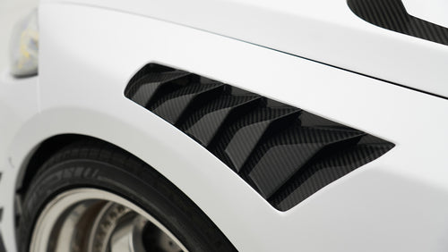 White BMW G80 M3 featuring a REVOZPORT carbon fiber body kit with front lip, side skirts, canards, vented fenders, and yellow DRL headlights displayed in a clean studio setting.