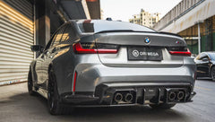 Gray BMW G80 M3 featuring a REVOZPORT carbon fiber front lip, side skirts, and aggressive aero styling parked outside a modern urban garage.