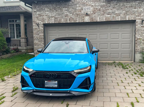 Blue Audi RS7 fitted with a REVOZPORT carbon fiber front lip and aggressive front aero styling, parked in an outdoor parking lot.