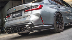 Gray BMW G80 M3 featuring a REVOZPORT carbon fiber front lip, side skirts, and aggressive aero styling parked outside a modern urban garage.