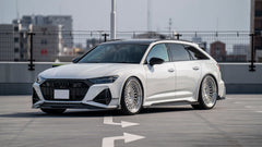 White Audi RS6 Avant featuring a REVOZPORT carbon fiber body kit with front lip, side skirts, rear diffuser, and lowered stance driving at high speed on a highway.