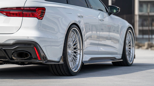 White Audi RS6 Avant featuring a REVOZPORT carbon fiber body kit with front lip, side skirts, rear diffuser, and lowered stance driving at high speed on a highway.