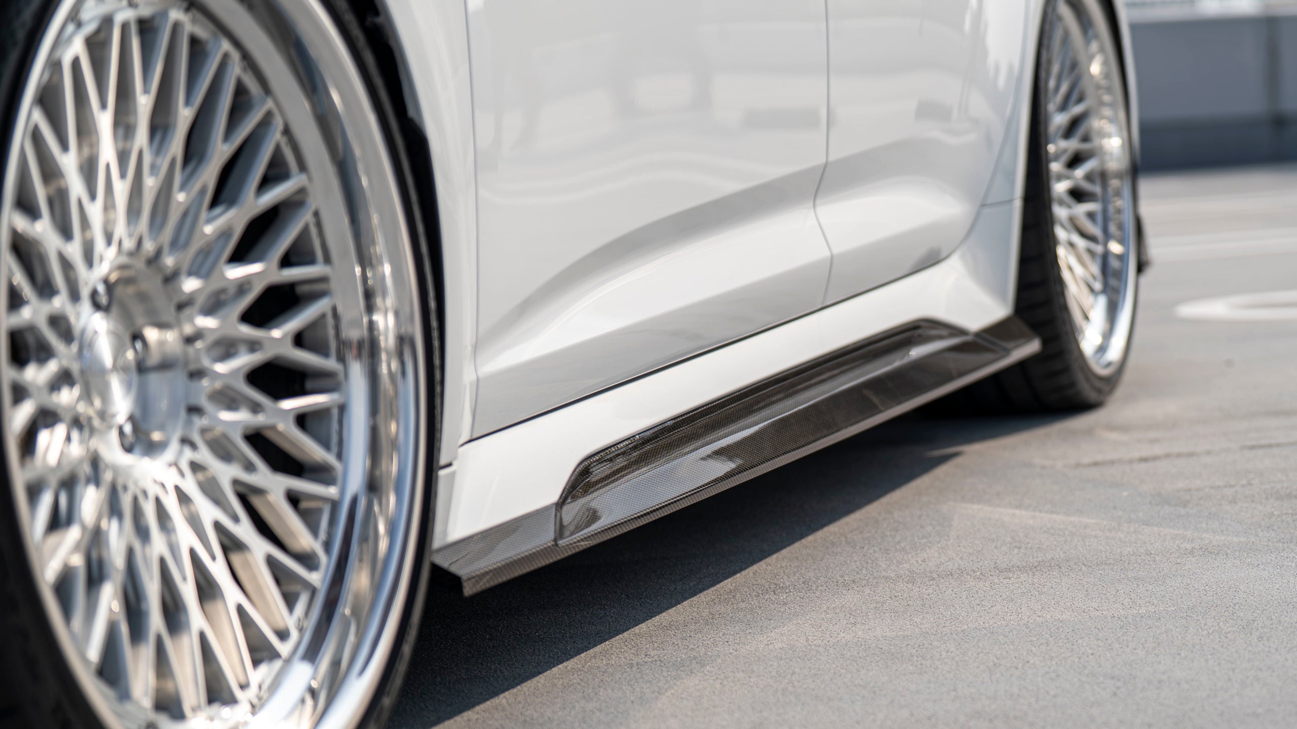White Audi RS6 Avant featuring a REVOZPORT carbon fiber body kit with front lip, side skirts, rear diffuser, and lowered stance driving at high speed on a highway.